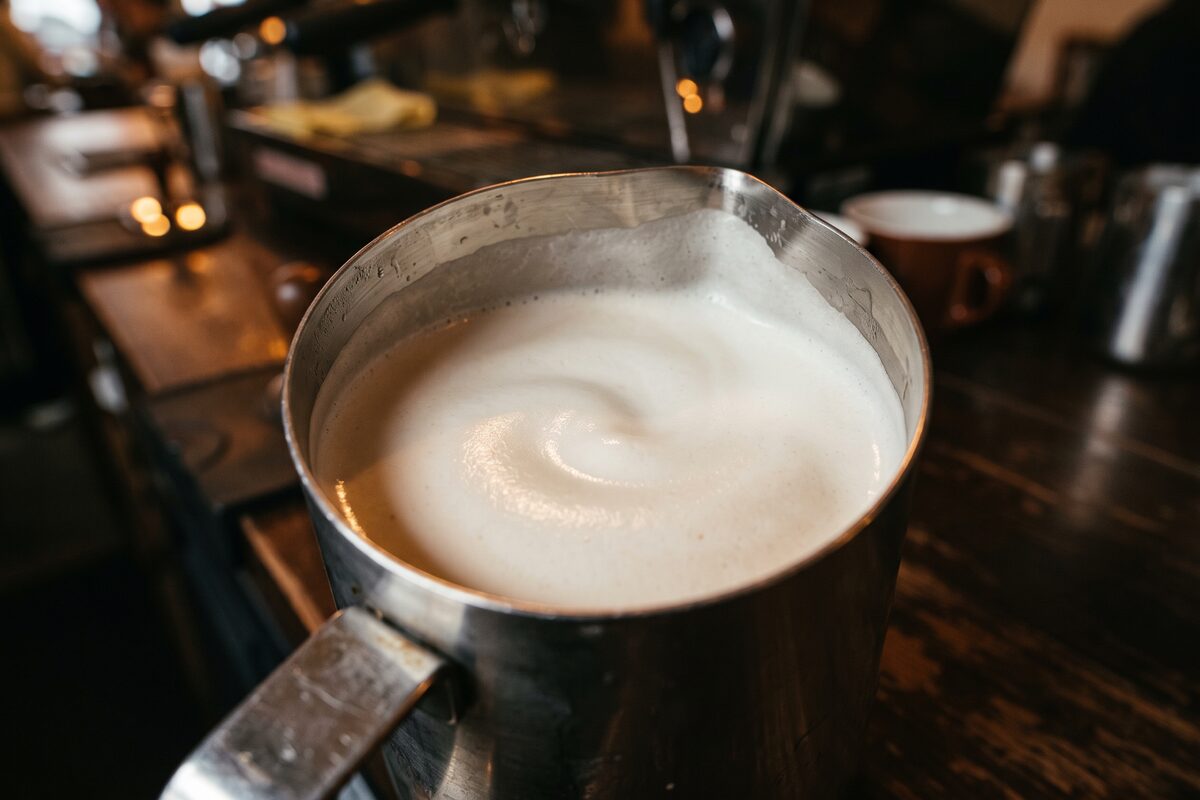 Close-up of dense, even milk microfoam in a steaming pitcher, lit from the side